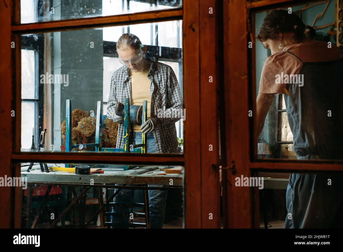 Uomo e donna che lavorano in officina, fanno mobili, riutilizzano i vecchi materiali per un nuovo prodotto. Consapevolezza nel consumo. Piccola impresa familiare. Riciclaggio Foto Stock