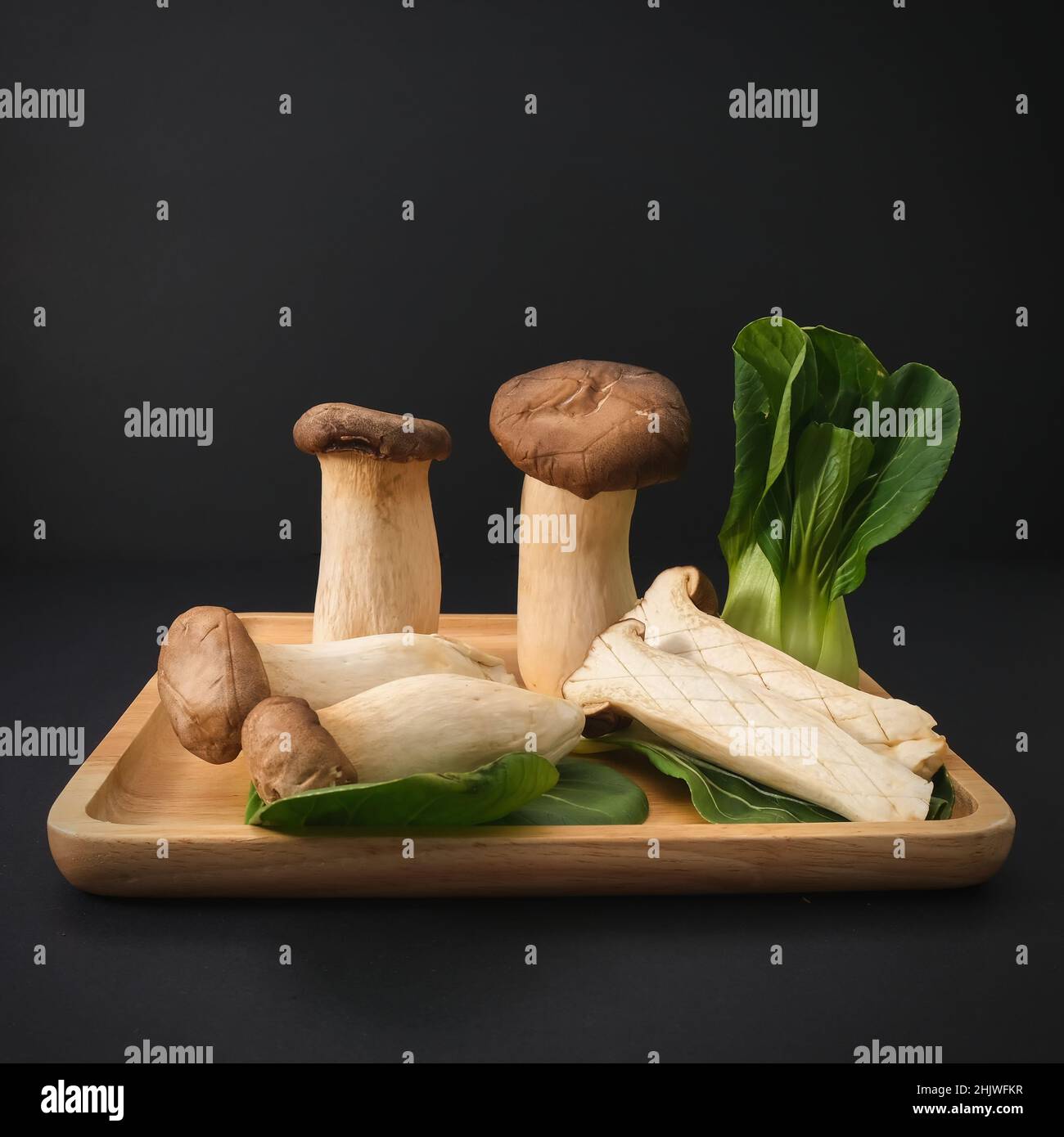 Popolari non cotti sani asiatici commestibili Re Oyster funghi e Baby Bok Choy su piatto di legno su sfondo nero. Foto Stock