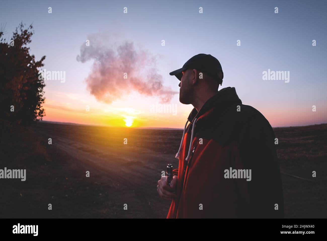 L'uomo fuma una sigaretta elettronica al tramonto Foto Stock