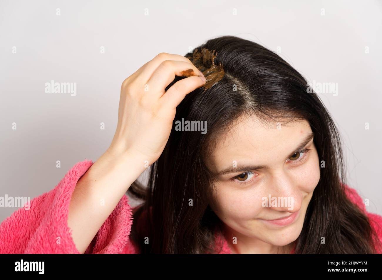 Una donna brunetta applica una miscela Ayurvedica naturale di erbe ai suoi capelli, maschera del cuoio capelluto e scrub, cura dei capelli a casa. Foto Stock