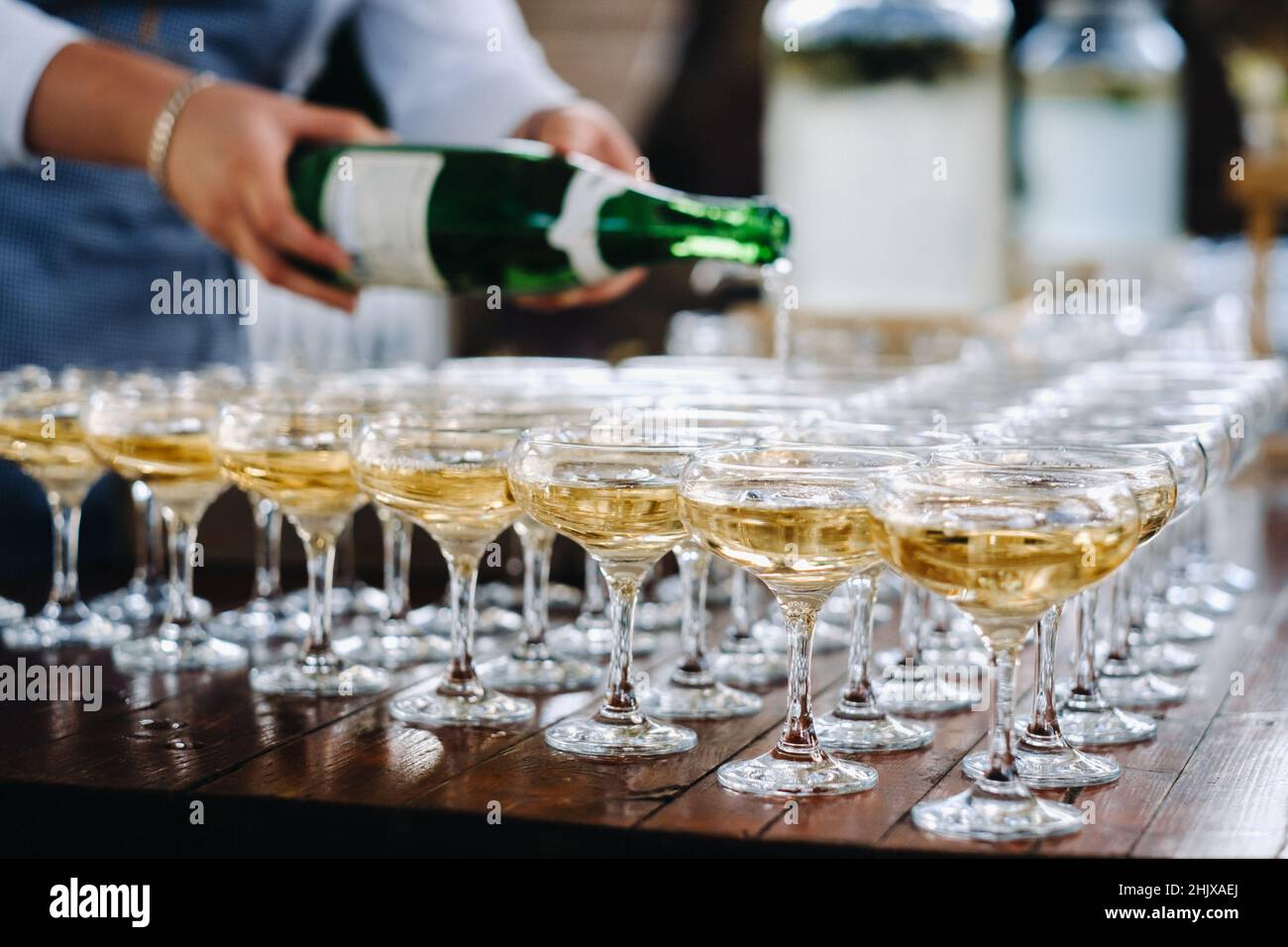 Barista versare champagne o vino in bicchieri di vino sul tavolo alla solenne cerimonia nuziale all'aperto. Foto Stock
