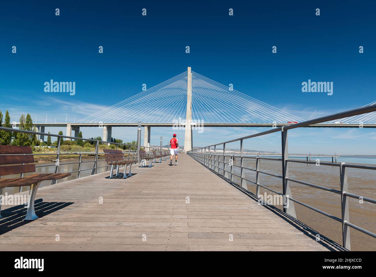 Corridore in camicia rossa sul Passeio do Tejo (Tour del Tago) che conduce al ponte Vasco da Gama. Parque das Nacoes / EXPO 98. Lisbona, Portogallo Foto Stock