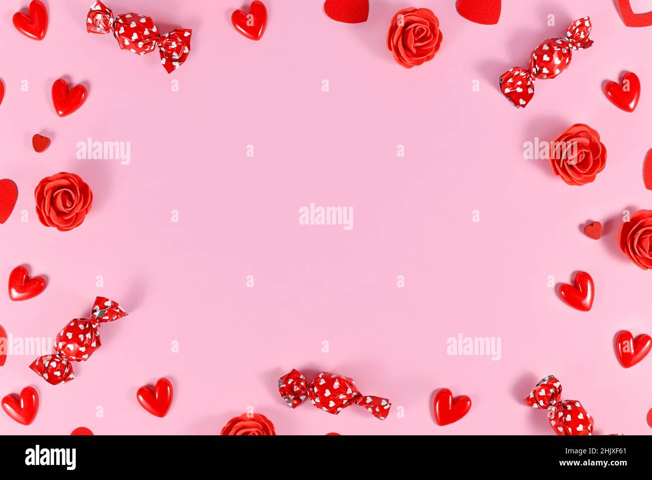 Caramelle di San Valentino, confetti a forma di cuore e rose rosse che formano la cornice intorno a sfondo rosa con spazio copia Foto Stock