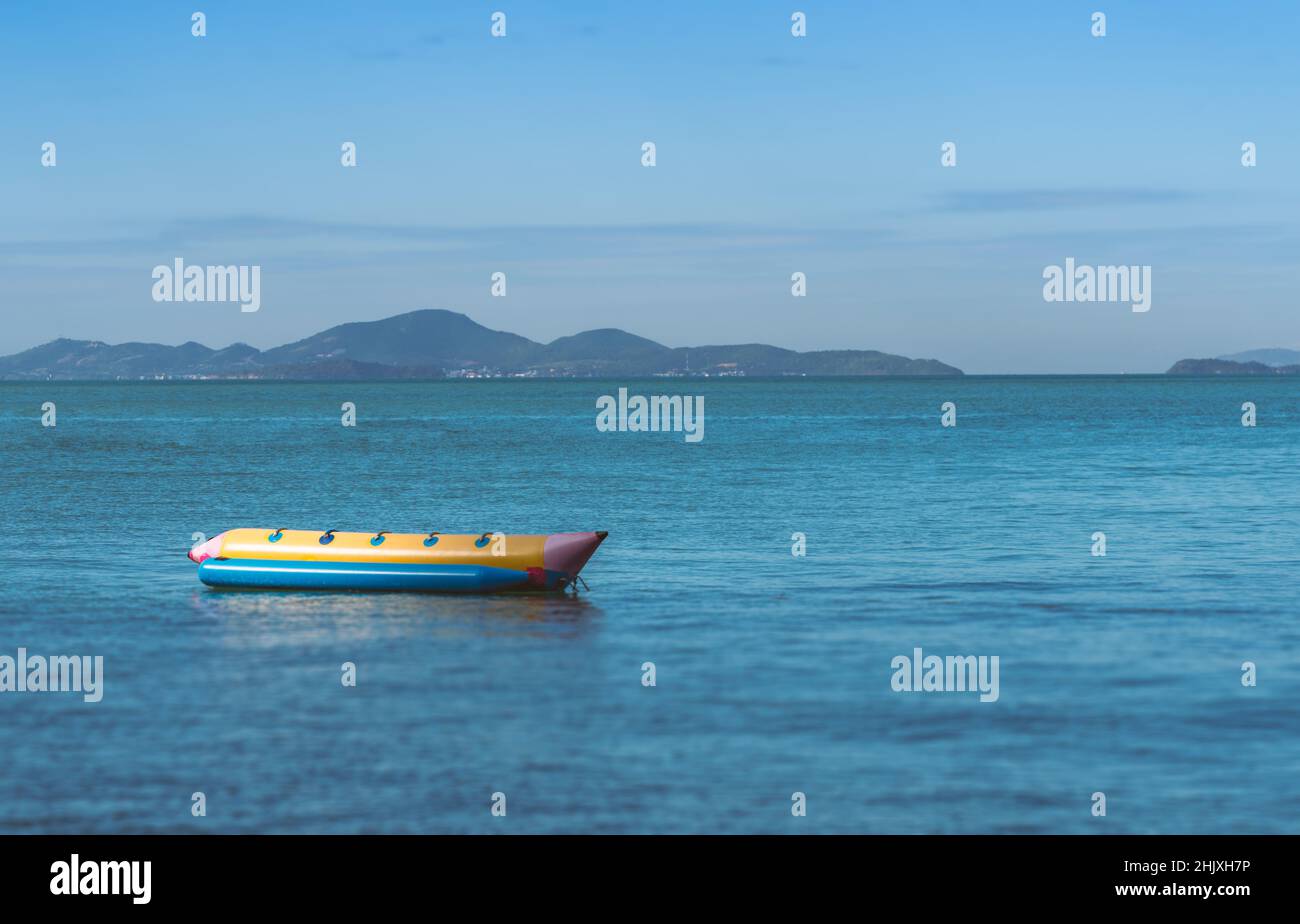Solitario Banana barca è galleggiante in mare a Pattaya in Thailandia, senza persone, vista sfondo di paesaggio di montagna e cielo, spazio vuoto per il testo e il design Foto Stock