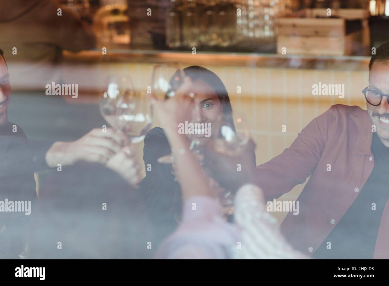 Amici maschi e femmine che tostano i wineglasses visto attraverso un bicchiere di bar Foto Stock