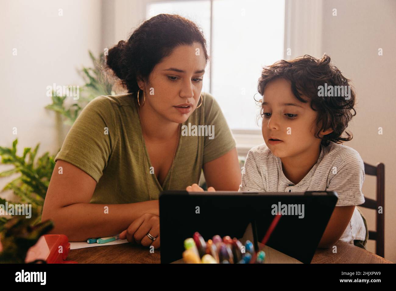 Madre di supporto che guarda un tutorial online con suo figlio. Madre e figlio che passano attraverso i contenuti educativi su un tablet digitale. Madre single amorevole Foto Stock