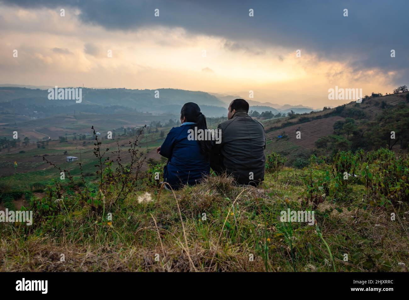 giovane coppia seduta sulla cima della montagna con sfondo nebbiosa della catena montuosa e il cielo drammatico al mattino immagine è scattata al picco della bamba shillong meghalaya indi Foto Stock