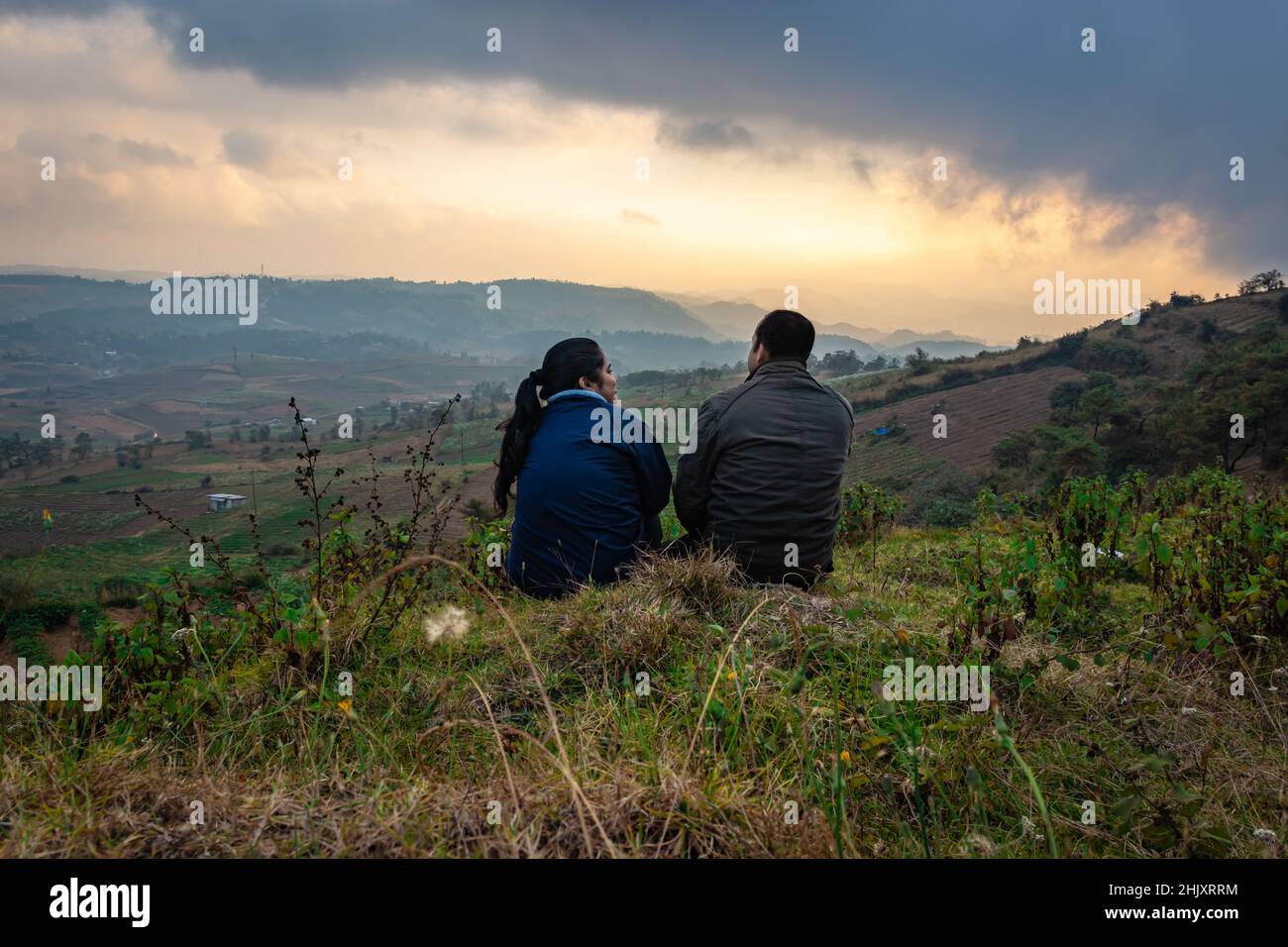 giovane coppia seduta sulla cima della montagna con sfondo nebbiosa della catena montuosa e il cielo drammatico al mattino immagine è scattata al picco della bamba shillong meghalaya indi Foto Stock