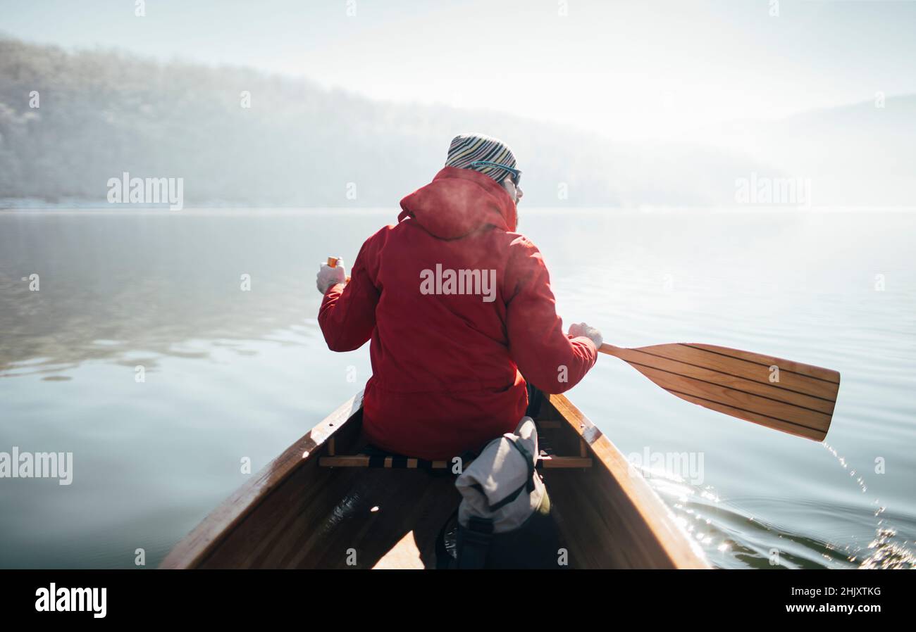 Vista posteriore della canoa uomo pagaiante nella giornata di sole d'inverno Foto Stock