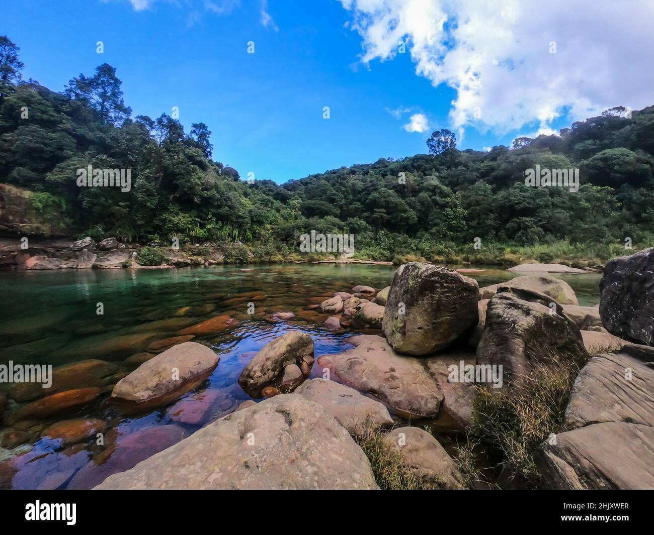 rocce che conducono al fiume acqua limpida circondato da foreste e cielo blu brillante immagine presa a lyngksair cascate meghalaya. Foto Stock