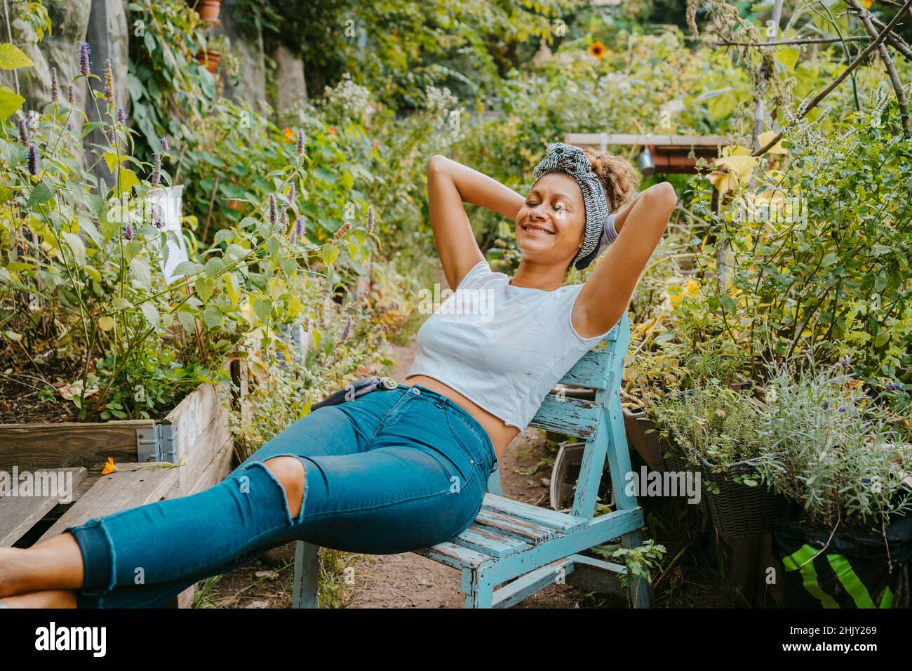 Donna contadina sorridente con le mani dietro la testa che riposa nel giardino urbano Foto Stock