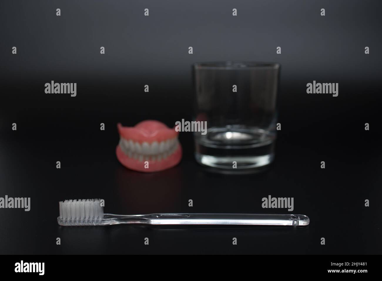 Dentiera completamente rimovibile in plastica delle ganasce. Due protesi acriliche. Cura dei denti con uno spazzolino. Denti e spazzolino su sfondo scuro. T suono Foto Stock
