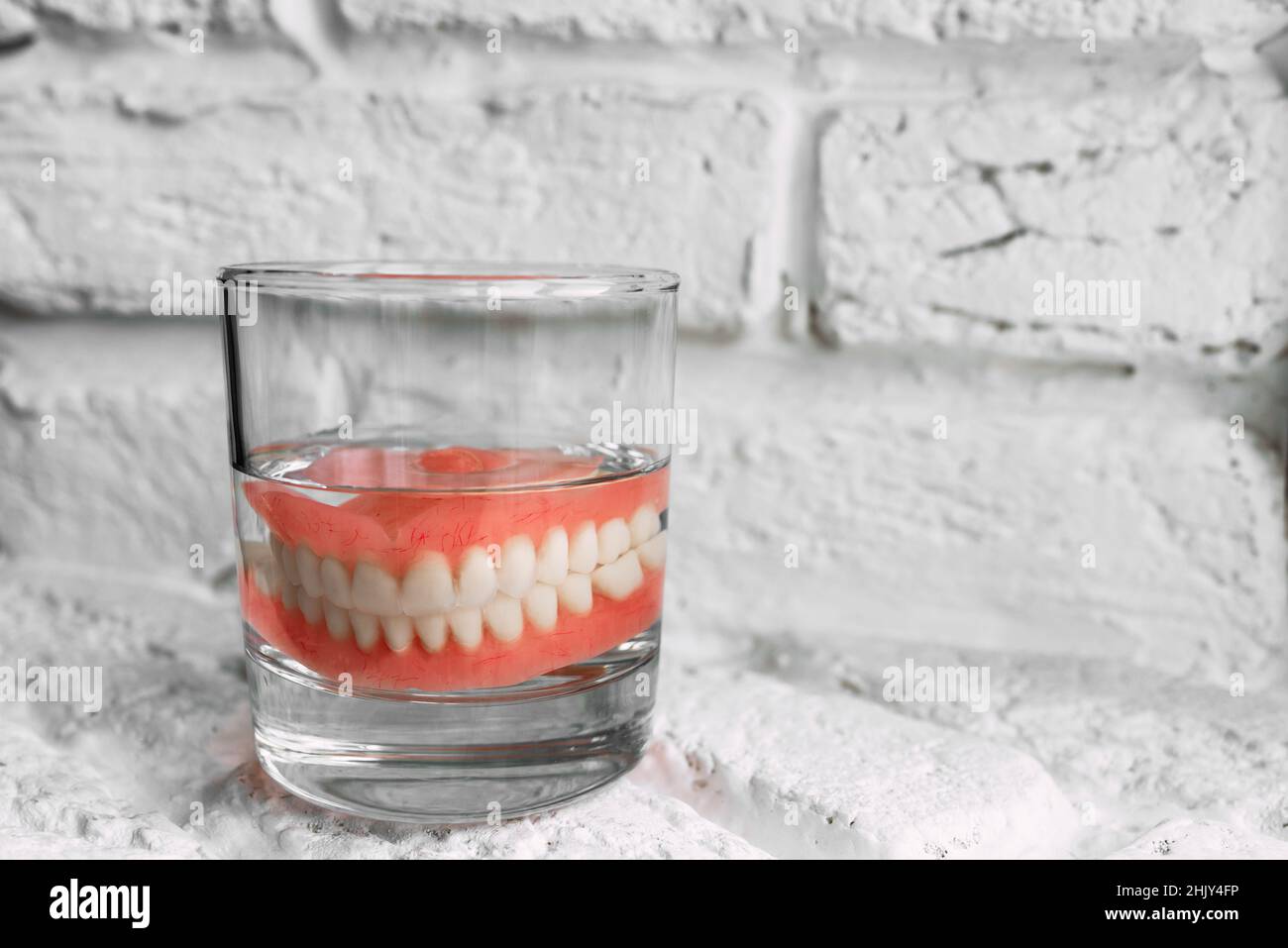 Una dentiera in un bicchiere d'acqua. Cura delle protesi dentarie. Dentiera  completamente rimovibile in plastica delle ganasce. Due protesi acriliche.  Ganasce superiore e inferiore con fak Foto stock - Alamy