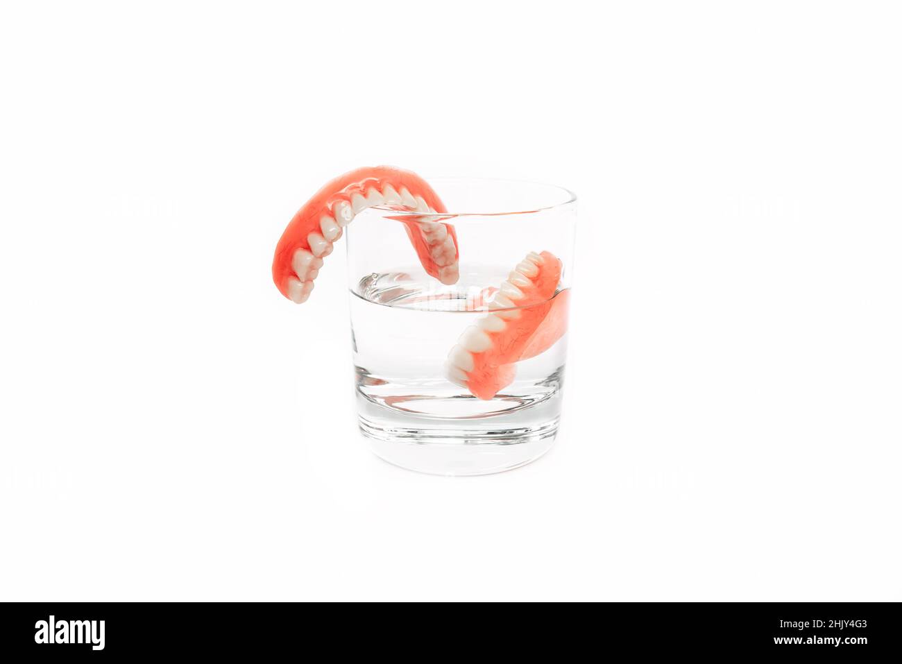 Cura delle protesi dentarie. Dentiera completamente rimovibile in plastica delle ganasce. Una serie di protesi in un bicchiere d'acqua su sfondo bianco. Due protesi acriliche. Foto Stock