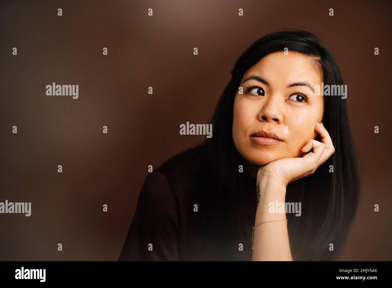 Donna contemplativa con mano sul mento in studio Foto Stock