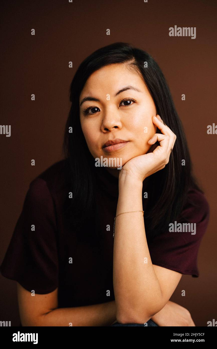 Ritratto di donna con mano sul mento su sfondo marrone Foto Stock