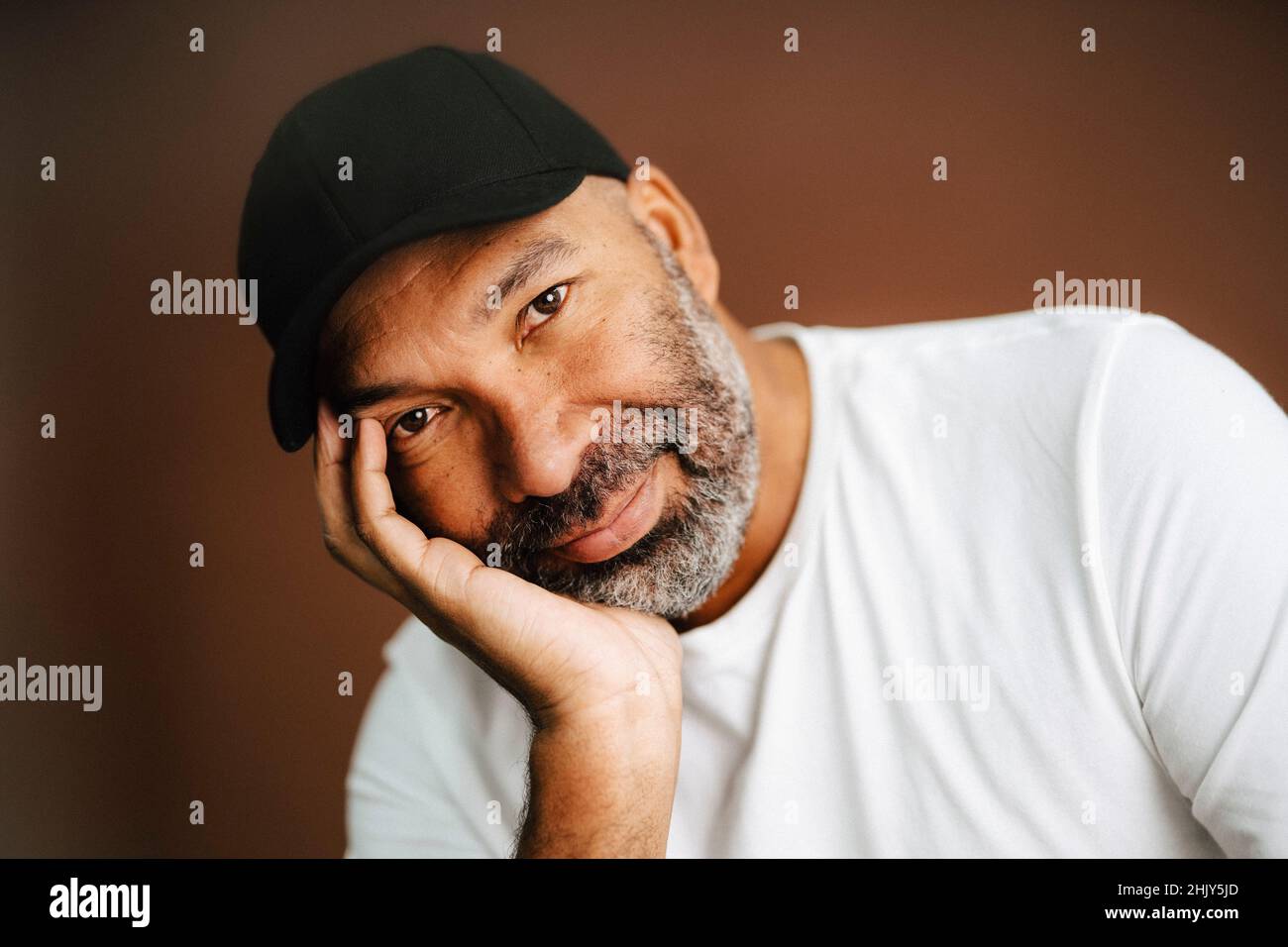 Uomo maturo con mano sul mento su sfondo marrone Foto Stock