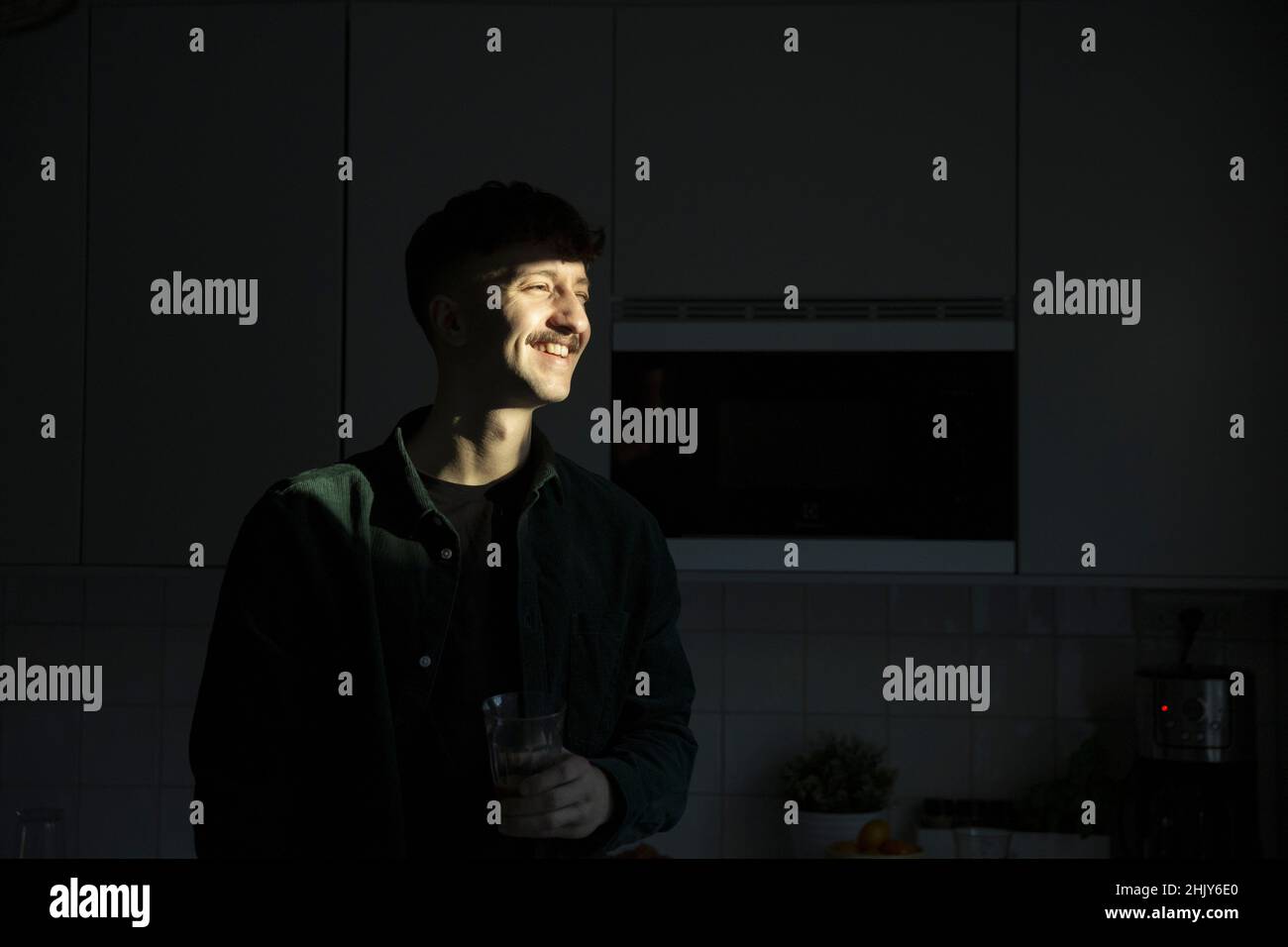 Uomo sorridente con luce del sole sulla faccia in piedi in cucina Foto Stock
