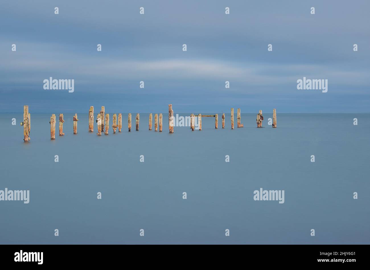Un'immagine minimalista del vecchio molo Swanage Dorset si erge nel mare ancora blu e nel cielo blu con una velocità dell'otturatore lenta Foto Stock