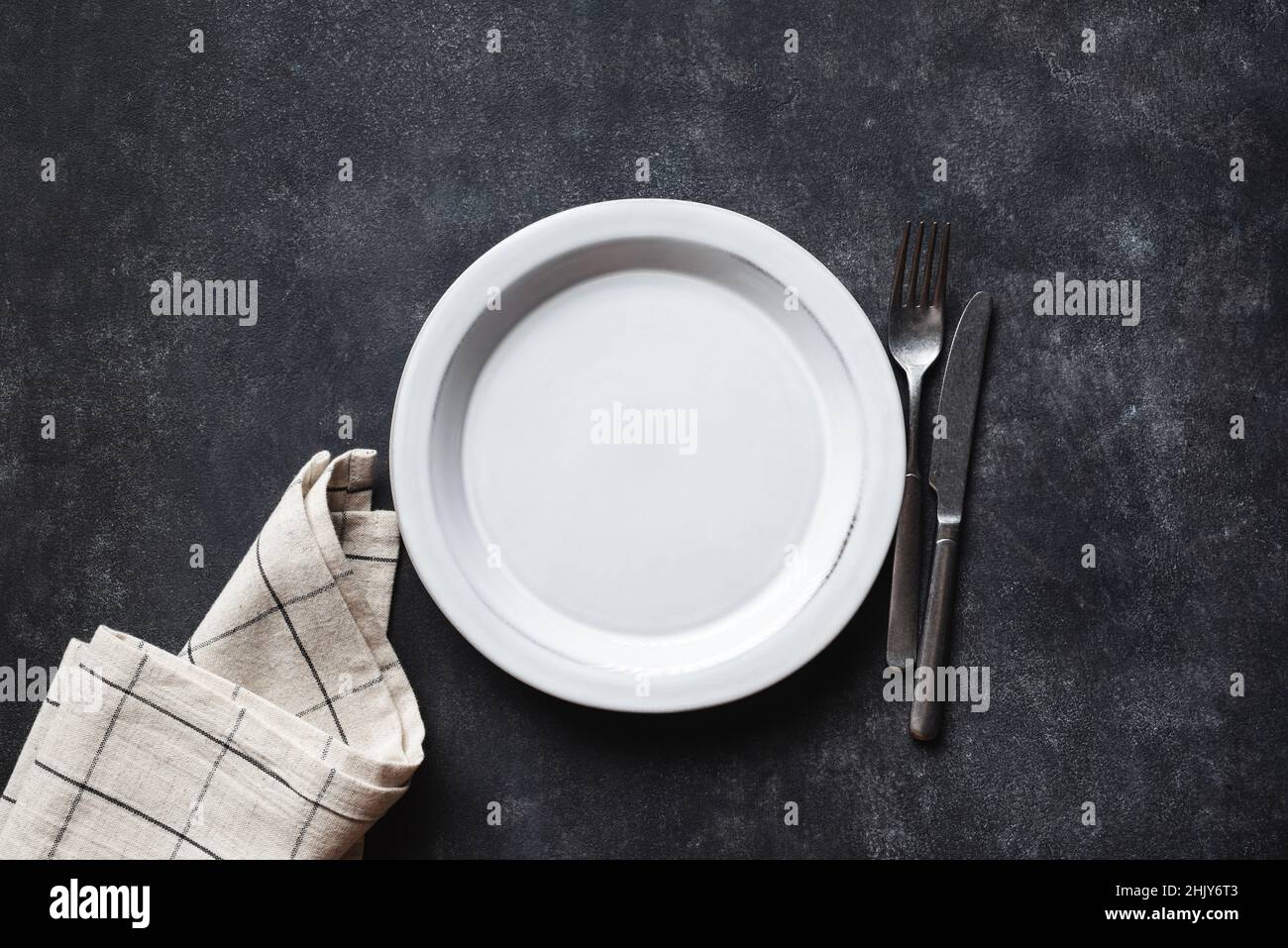 Piatto vuoto, posate e biancheria da tavola su fondo piano in cemento nero. Vista dall'alto dello spazio di copia. Tavolo da cucina Foto Stock