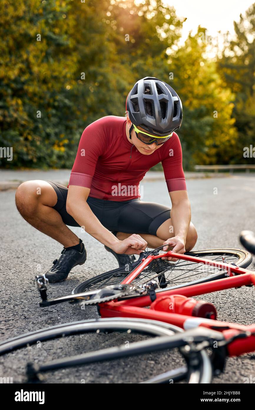 Il ciclista sportivo ripara le parti e si regola da solo sulla strada. All'aperto. Atleta forte in sportswear e casco è impegnato in healt Foto Stock