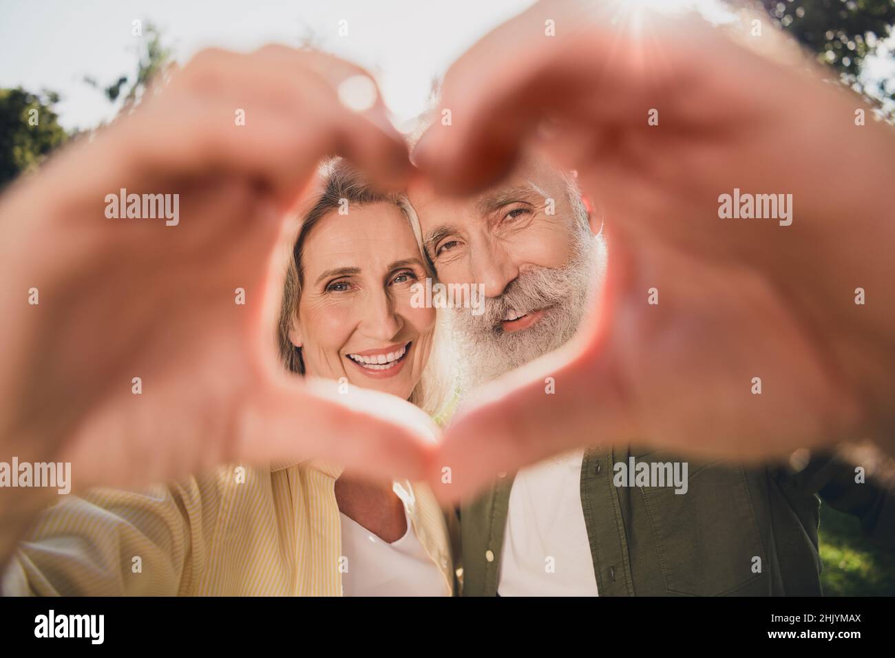 Foto di una bella coppia di anziani mostra cuore indossare camicia passeggiata nel parco all'aperto Foto Stock