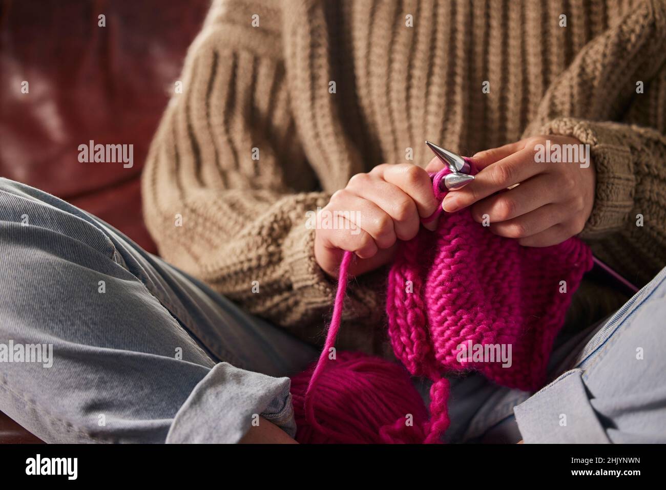 Primo piano di donna seduta sul divano a casa maglia ponticello con lana rosa Foto Stock