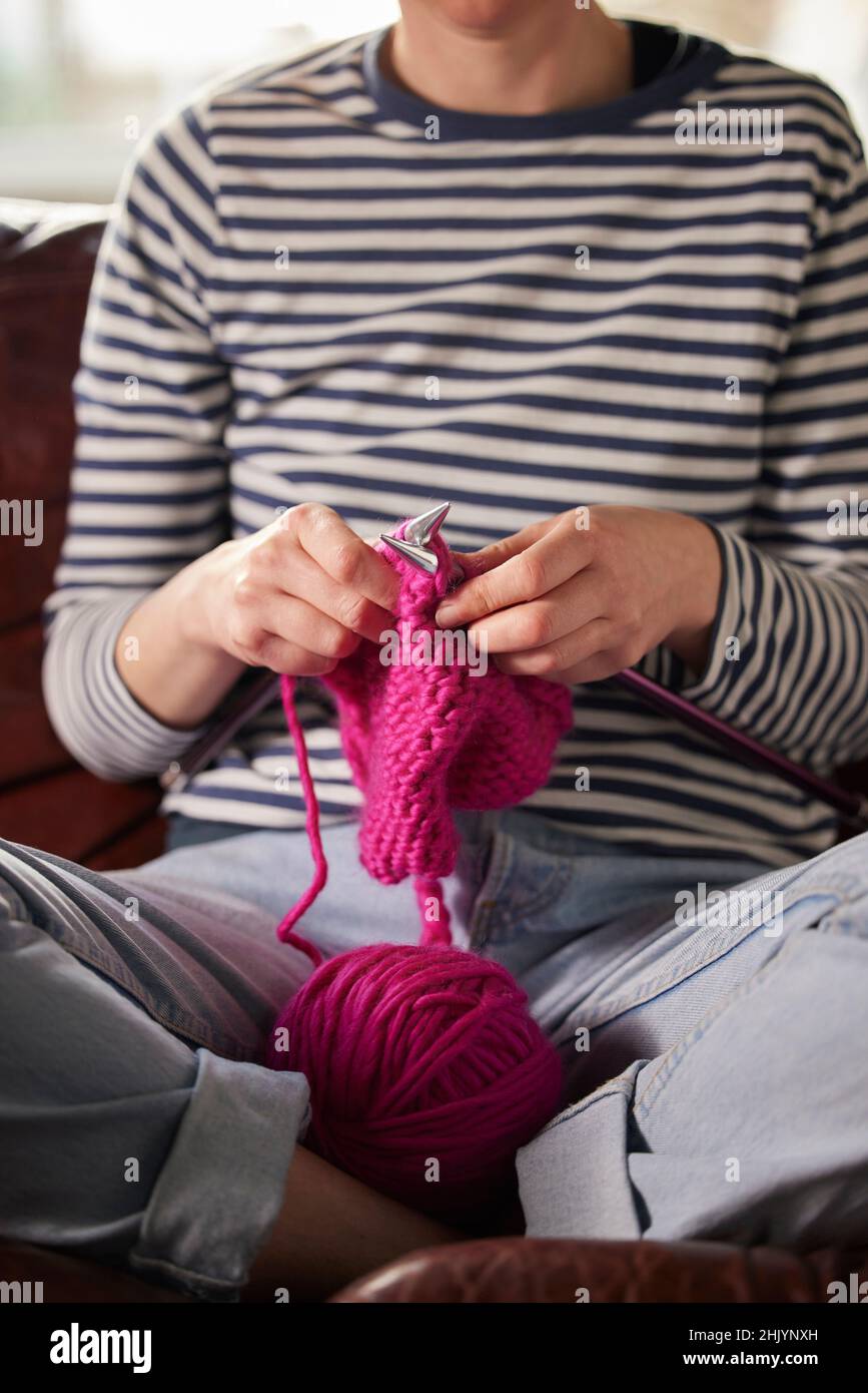 Primo piano di donna seduta sul divano a casa maglia ponticello con lana rosa Foto Stock