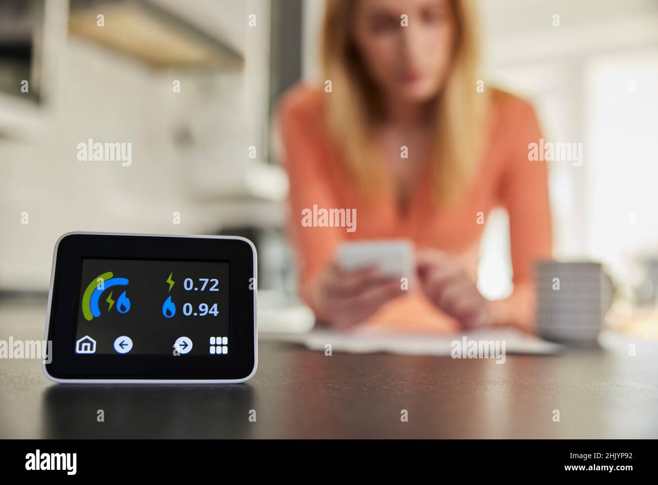 Primo piano del contatore di energia intelligente in cucina misurazione dell'uso di elettricità e gas con la donna guardando le fatture con il calcolatore Foto Stock