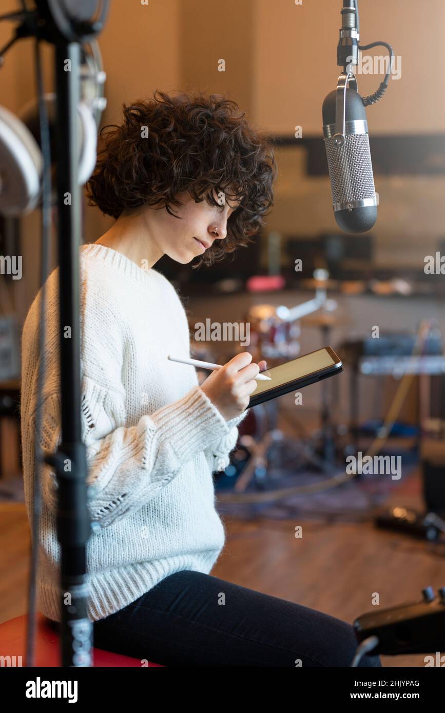 Giovane donna con capelli ricci seduti e pensando a cosa scrivere nello studio di musica Foto Stock
