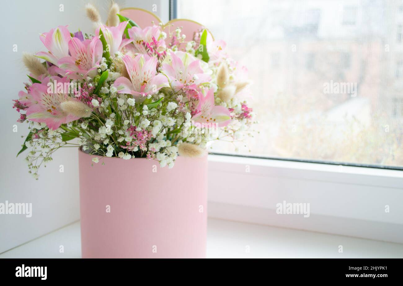 Delicato bouquet di gigli rosa, rose bianche in una confezione regalo sulla finestra. Biglietto di auguri. Spazio di copia. Foto Stock