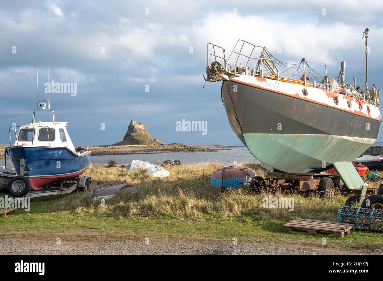 Barche da pesca ormeggiate nel porto sulla Holy Island di Lindisfarne, Northumberland, Regno Unito, con il castello in prossimità. Foto Stock