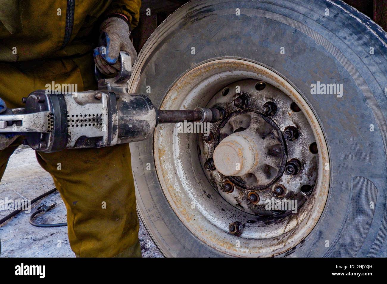 un addetto alla riparazione di pneumatici svita le ruote di un veicolo pesante con una chiave pneumatica, Foto Stock