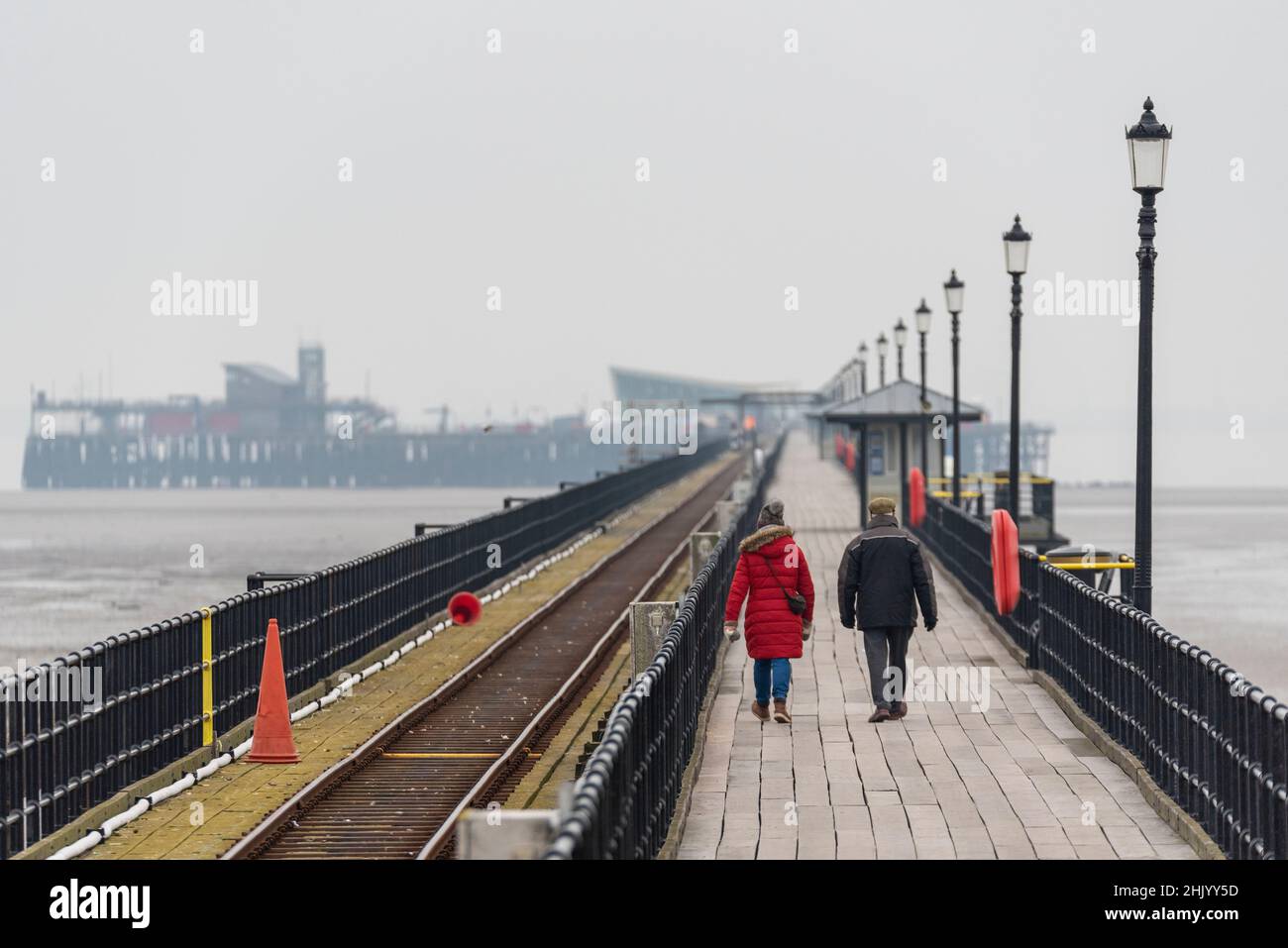 Coppia che inizia la lunga passeggiata a Southend Pier, Southend on Sea, Essex, Regno Unito, su un nebby, freddo, mattina d'inverno. Avvolti contro il freddo. Distanza Foto Stock