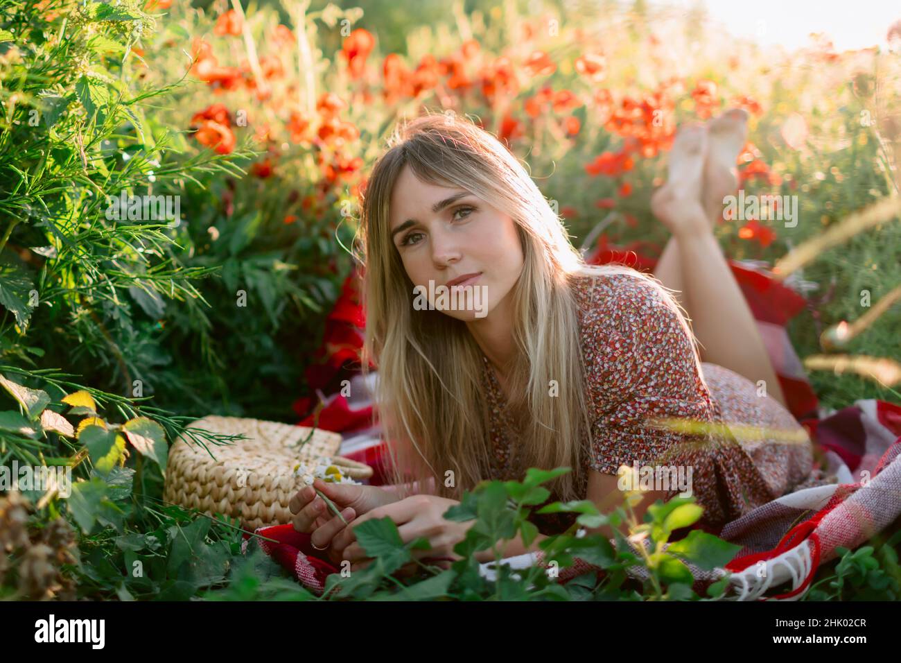 Ritratto donna all'aperto in plaid con fiori di papavero al tramonto. Donna in abito e borsa con fiori da campo Foto Stock