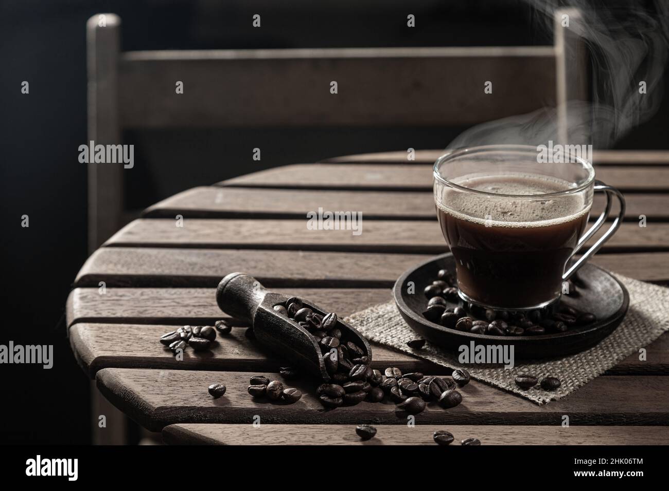 Caffè caldo in una tazza di vetro e chicchi di caffè su un tavolo di legno su sfondo scuro. Foto Stock
