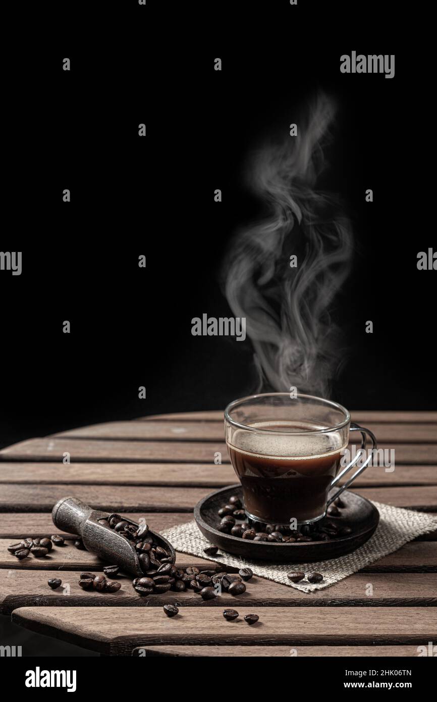 Caffè caldo a vapore in una tazza di vetro e chicchi di caffè su sfondo nero. Formato verticale. Foto Stock