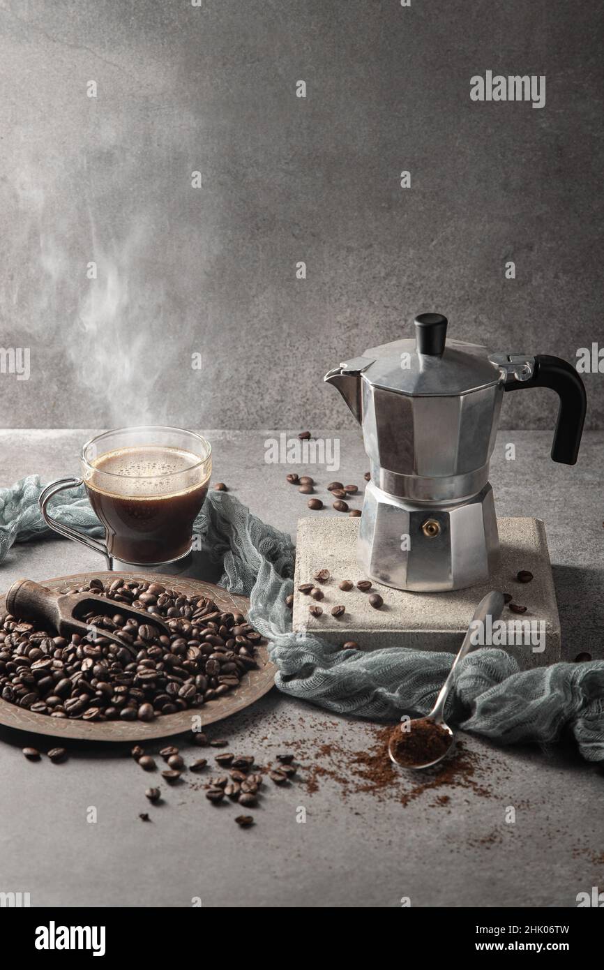 Caffè caldo in una tazza di vetro e chicchi di caffè su sfondo chiaro. Formato verticale. Foto Stock