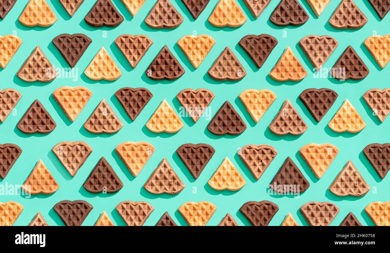 Molti waffle a forma di cuore allineati su uno sfondo verde, vista dall'alto. Potrai gustare deliziosi waffle a base di cacao, vaniglia e cinnamo Foto Stock