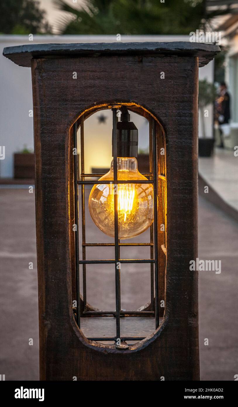 Lanterna rustica in legno con lampadina a LED che brilla al crepuscolo. Stile rustico illuminato per aree all'aperto. Foto Stock