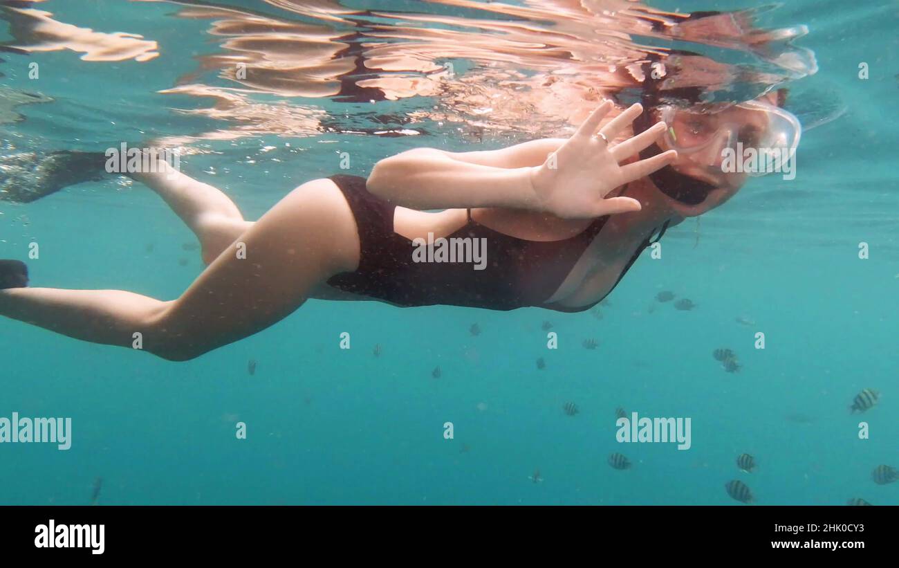 Saluti dal mondo sotterraneo. 4k filmati video di una giovane donna attraente che sventolano e salutano mentre nuotano nell'oceano blu profondo. Foto Stock