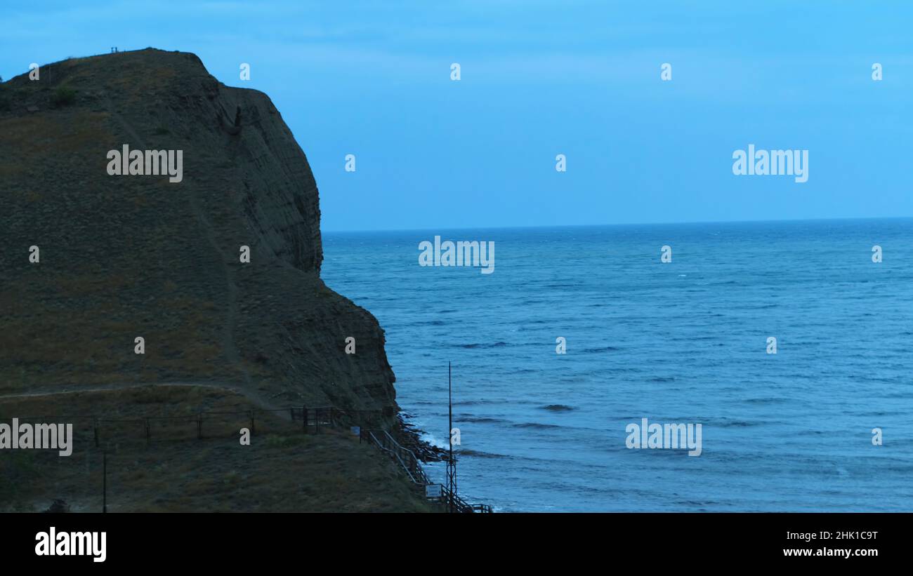 Vista aerea della grande scogliera grigia e delle onde di mare che si infrangono sulle rocce contro il cielo blu della sera. Splendido scenario marino serale Foto Stock