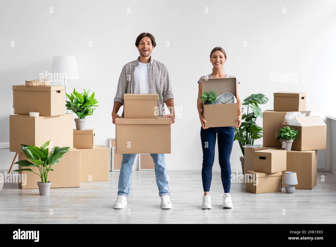 Soddisfatto millenario caucasico maschio e femmina Carry scatole e piante in camera interno e godere di muoversi a casa propria Foto Stock