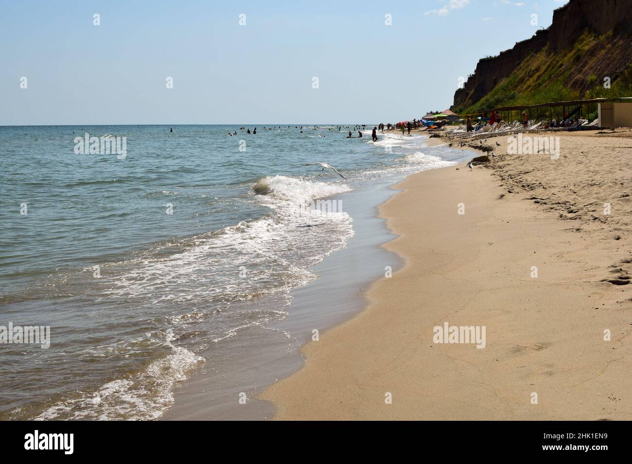Le onde di mare schiumose rotolano sulla spiaggia di sabbia diurna. I turisti si prendono il sole e nuotano in lontananza Foto Stock