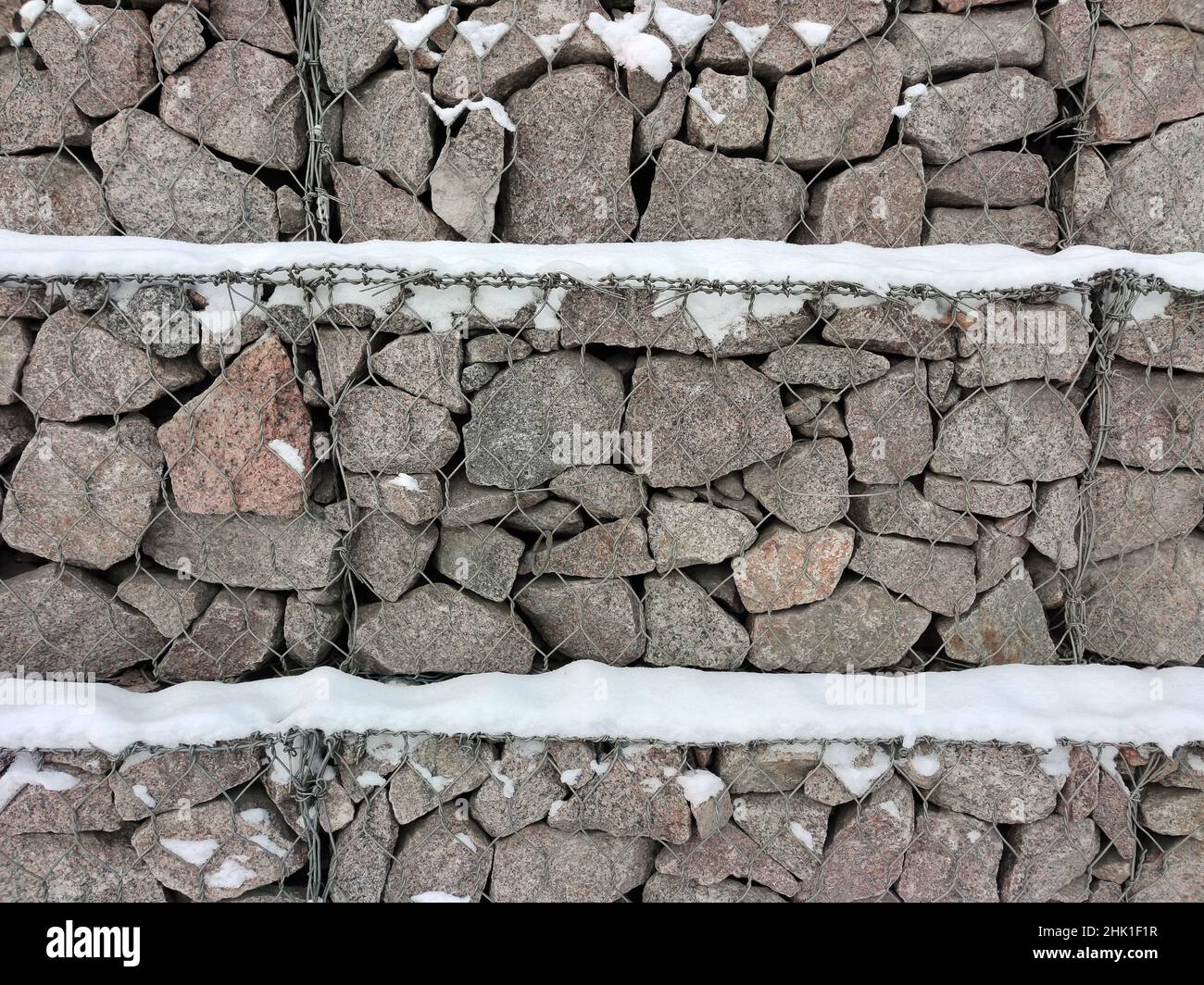 Un muro di massi di pietra irregolari tenuti insieme con filo di ferro e cosparsi di neve bianca Foto Stock