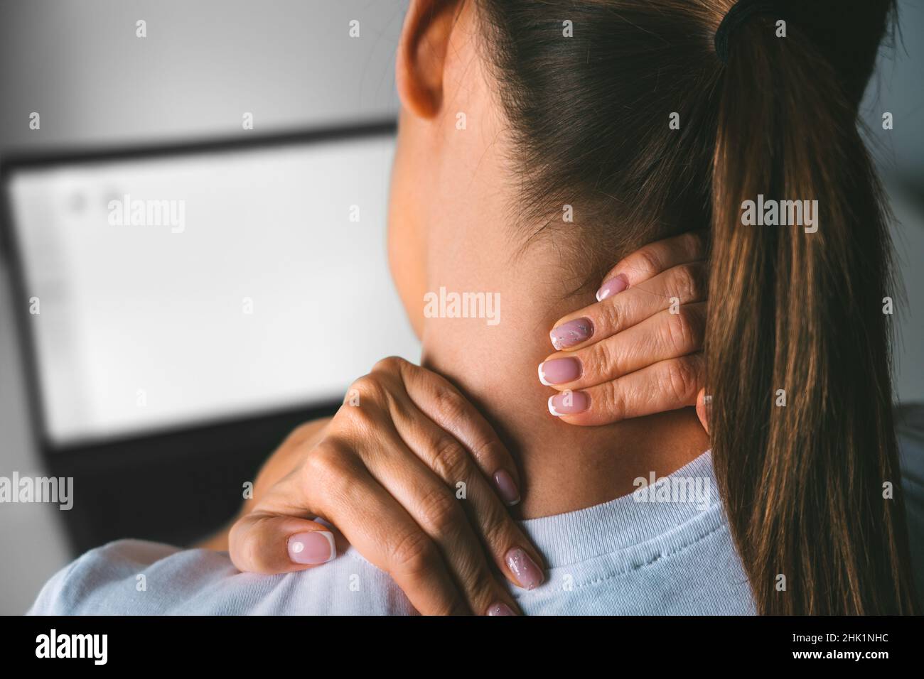 Giovane donna che soffre di dolore al collo dopo aver lavorato sul pc e massaggiando il collo per alleviare il dolore Foto Stock