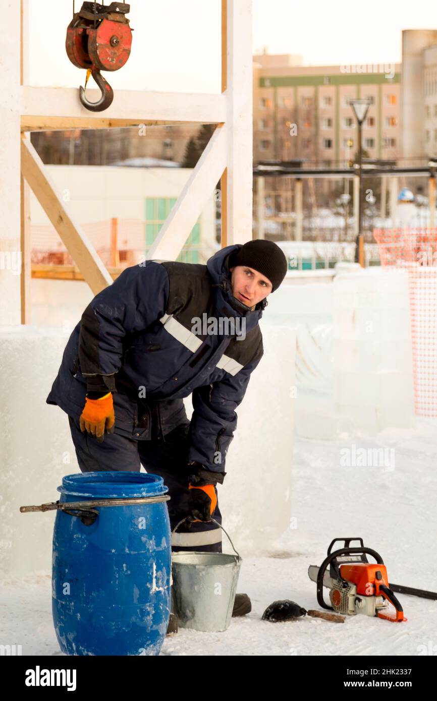 Un lavoratore con un secchio in mano vicino ad un barile blu nel luogo di assemblaggio della città di ghiaccio Foto Stock