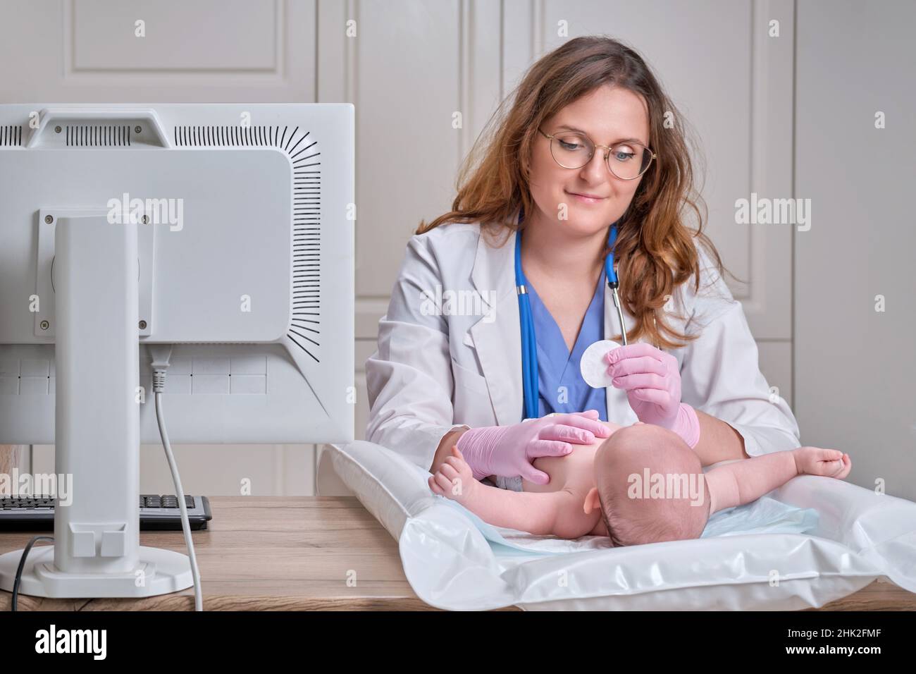 Il medico si occupa dell'igiene del naso e degli occhi del neonato con un batuffolo di cotone. L'infermiera in uniforme sfrega la pelle di un bambino Foto Stock