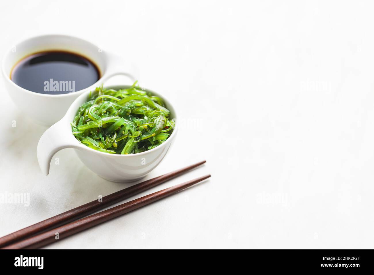 Wakame verde. Insalata di alghe e salsa di soia in ciotola su tavola bianca. Foto Stock
