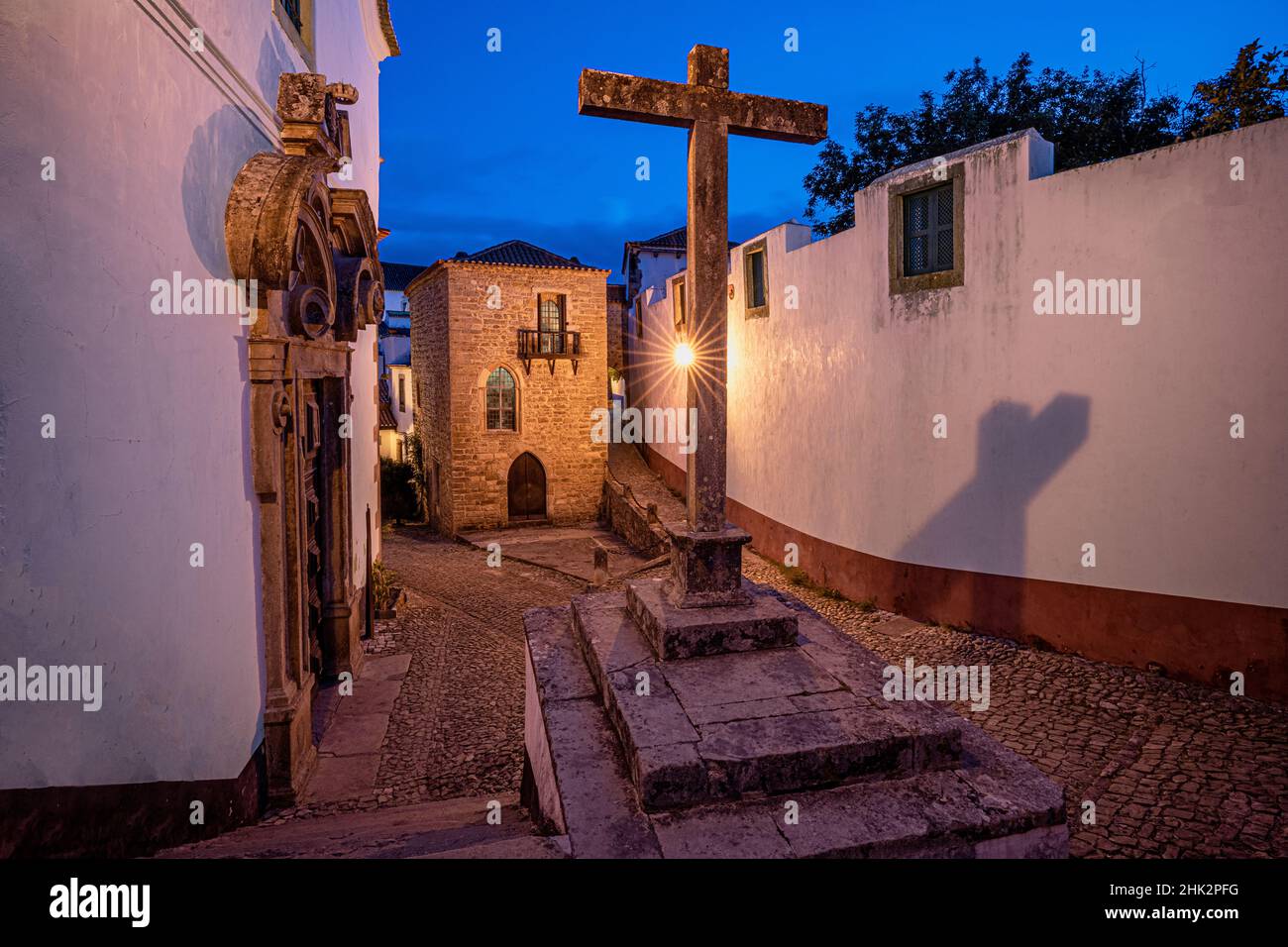 Europa, Portogallo, Obidos. Chiesa e attraversare su strada acciottolata al tramonto. Foto Stock